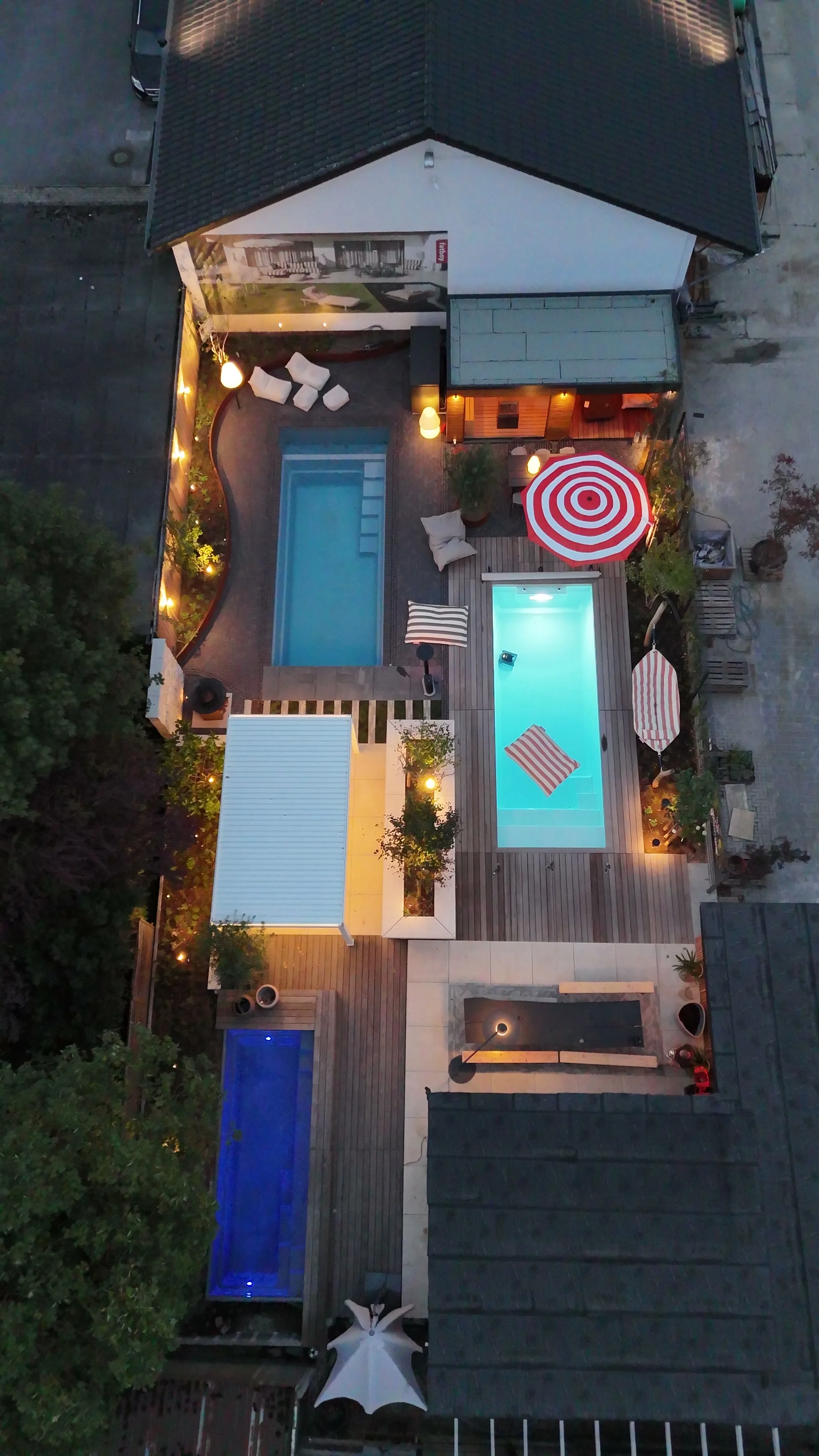 Die Ausstellung senkrecht von oben am Abend: zwei beleuchtete Becken, Pergola, Holzdeck, Sonnenschirm und Sitzecke.
