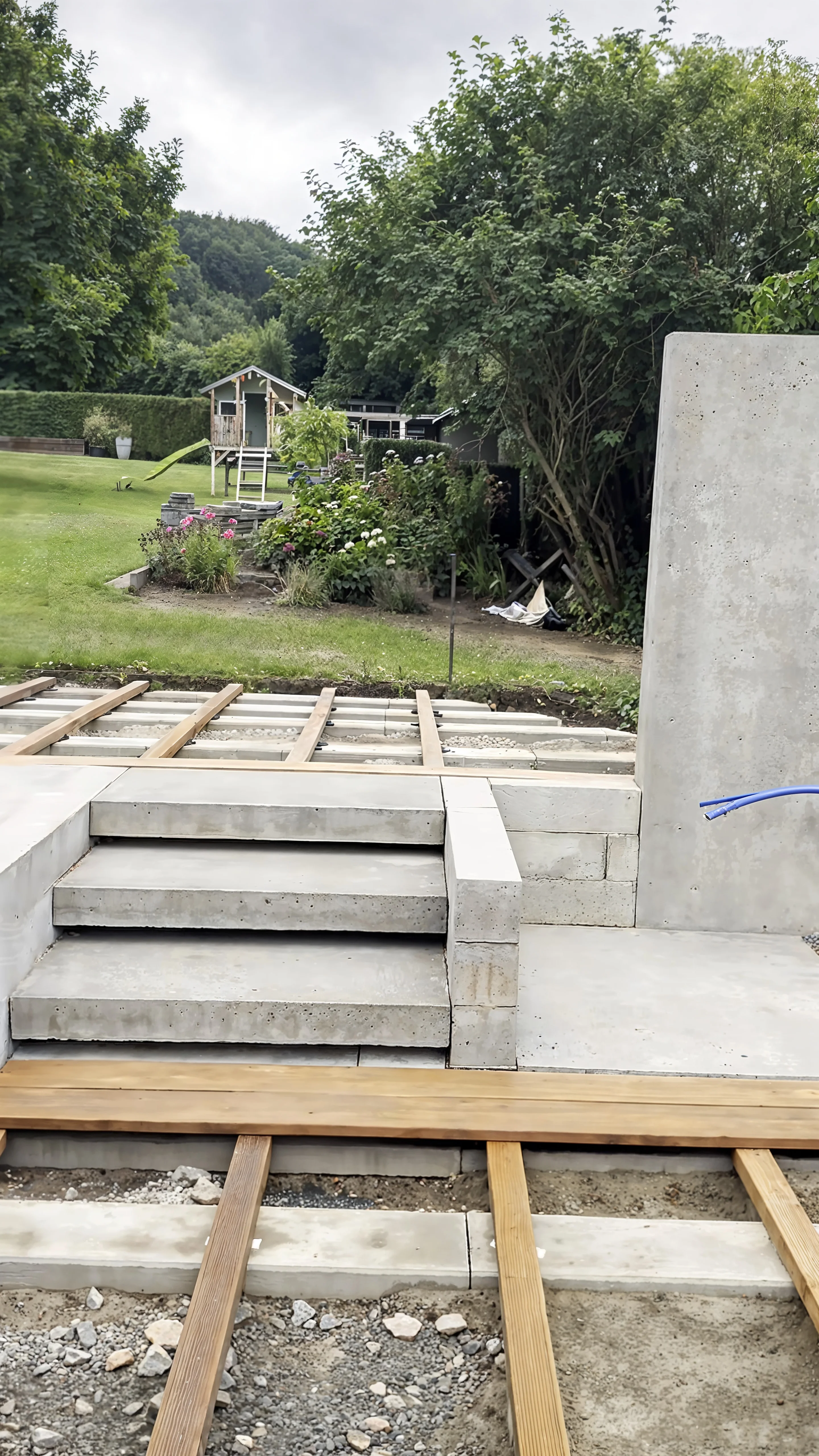 Baustelle: Betonstufen und Mauer stehen, die Unterkonstruktion des Holzdecks liegt auf dem Schotter.